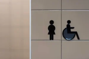 Raised tactile pictogram signage for women's restroom and wheelchair accessible symbol, an example of ADA-compliant interior signage